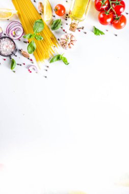 Makarna pişirmek için İtalyan yemekleri. Çeşitli malzemeli çiğ spagetti makarna - soğan, domates, sarımsak, fesleğen, maydanoz, peynir, zeytinyağı. Beyaz tablo arkaplanında, düz kopya alanı