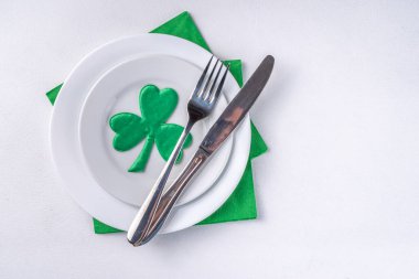 St. Patrick's Day festive table setting. Plate and cutlery with green napkin, shamrock symbol, gold horseshoe decor for luck. Patrick Day menu background, party invitation, top view copy space