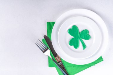 St. Patrick's Day festive table setting. Plate and cutlery with green napkin, shamrock symbol, gold horseshoe decor for luck. Patrick Day menu background, party invitation, top view copy space