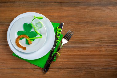 St. Patrick's Day festive table setting. Plate and cutlery with green napkin, shamrock symbol, gold horseshoe decor for luck. Patrick Day menu background, party invitation, top view copy space