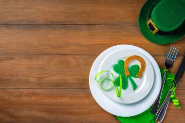 St. Patrick's Day festive table setting. Plate and cutlery with green napkin, shamrock symbol, gold horseshoe decor for luck. Patrick Day menu background, party invitation, top view copy space