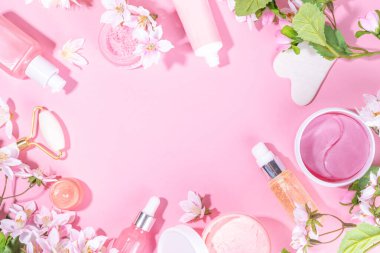 Spring skin care cosmetics flat lay.  Beauty facial care cosmetics: serum, cream, mask on pink sunny background with spring blossom flowers, top view copy space