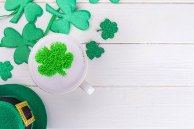 Aziz Patrick Günü için basit bir geçmiş. Süt köpüklü kapuçino latte kahve ve beyaz ahşap arka planda dört yapraklı yeşil şeker tozu yoncası dekoru.