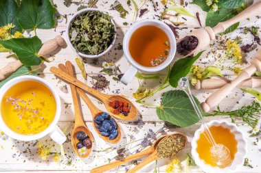 Sağlıklı içecekler, bitkiler ve çiçek konsepti. Taze ve kurutulmuş organik bitkisel çay çeşitleri, beyaz ahşap masa üzerinde demlenmiş sıcak çay fincanları.