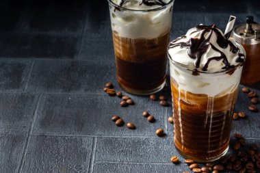 Soğuk kahve içen frappe (frappuccino), krema ve çikolata şurubuyla, pipetlerle, kahve çekirdekleri koyu gri bir taş masada, boşluğu kopyala 