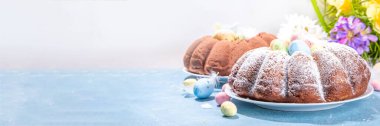 Traditional cake for Easter. Chocolate and vanilla Easter round cake with chocolate and sugar powder sprinkles, colorful Easter eggs, spring flowers, on a blue background copy space