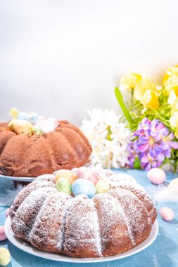 Traditional cake for Easter. Chocolate and vanilla Easter round cake with chocolate and sugar powder sprinkles, colorful Easter eggs, spring flowers, on a blue background copy space
