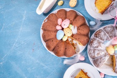 Traditional cake for Easter. Chocolate and vanilla Easter round cake with chocolate and sugar powder sprinkles, colorful Easter eggs, spring flowers, on a blue background copy space