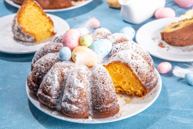 Traditional cake for Easter. Chocolate and vanilla Easter round cake with chocolate and sugar powder sprinkles, colorful Easter eggs, spring flowers, on a blue background copy space