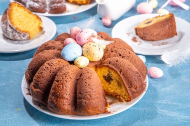 Traditional cake for Easter. Chocolate and vanilla Easter round cake with chocolate and sugar powder sprinkles, colorful Easter eggs, spring flowers, on a blue background copy space