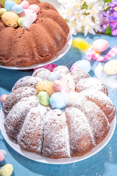 Traditional cake for Easter. Chocolate and vanilla Easter round cake with chocolate and sugar powder sprinkles, colorful Easter eggs, spring flowers, on a blue background copy space