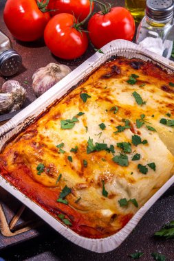 Homemade cannelloni pasta, big tray with baked cannelloni with minced meat with bechamel sauce,with herbs in ingredient on dark background