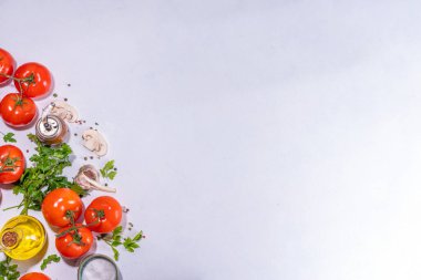 Cooking background with vegetable ingredients. Healthy dinner preparation flat lay, with fresh raw tomatoes, onion, garlic, herbs and greens, olive oil, salt, pepper seasonings, on white background 
