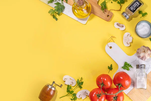 Cooking background with vegetable ingredients. Healthy dinner preparation flat lay, with fresh raw tomatoes, onion, garlic, herbs and greens, olive oil, salt, pepper seasonings, on yellow background