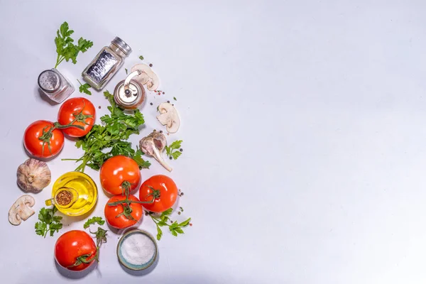 Cooking background with vegetable ingredients. Healthy dinner preparation flat lay, with fresh raw tomatoes, onion, garlic, herbs and greens, olive oil, salt, pepper seasonings, on white background