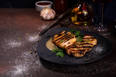 American bbq food concept. Grilled barbeque pork meat steaks with traditional gravy sauce, spices and greens, on plate board, dark background top view copy space 