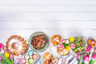 Festivalde Paskalya yemeği veya brunch masası sunuldu, Paskalya yumurtası, lale çiçeği buketi, geleneksel Paskalya yemekleri - pasta, çapraz çörekler, çelenk ekmeği, jöleli jambon ve bahar salatası, beyaz masa arkaplanı