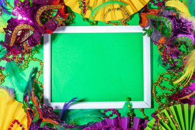 Mardi Gras colourful holiday greeting card background with festival masquerade accessories, decor, carnival mask, beads, feathers, fan on bright background traditional yellow purple green colors