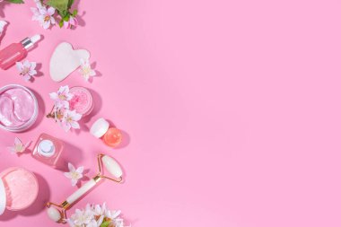 Spring skin care cosmetics flat lay.  Beauty facial care cosmetics: serum, cream, mask on pink sunny background with spring blossom flowers, top view copy space