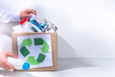 Çöp ayıklama, atık geri dönüşüm konsepti. Geri dönüşüm malzemelerinin olduğu kutu - plastik, cam, kağıt, karton, beyaz ahşap arka plan fotokopi alanı. Kadın elleri çeşitli çöp ve çöpleri ayırıyor.