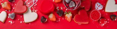 Various Valentine day sweets and desserts, cookies, chocolates, candy, sugar sprinkles with strawberry on high-colored bright red holiday background flatlay top view copy space