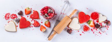 Valentine day baking background, Various bakery ingredients, cookies, chocolates, sugar sprinkles, strawberry, rolling pin and whisk, for cooking valentine`s sweets, desserts on white background