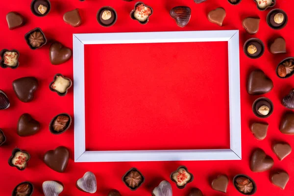 Valentines Day chocolates banner, background, frame. Various sweets and chocolate candy on red paper background with copy space. Romantic composition. Happy Valentine\'s day greeting card background