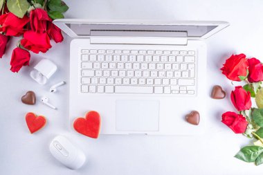 Woman using laptop with red roses. White laptop on white table background with chocolates, cookie hearts, red roses bouquet, flat lay working holiday, Valentine day background, top view copy space