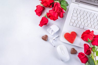 Woman using laptop with red roses. White laptop on white table background with chocolates, cookie hearts, red roses bouquet, flat lay working holiday, Valentine day background, top view copy space