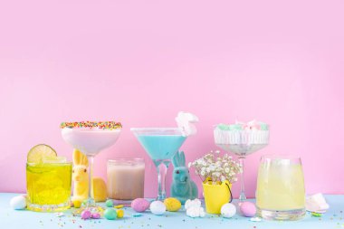 Colorful pastel colored kids Easter party mocktails, Creamy and iced non-alcohol drinks with cotton candy, marshmallow, sugar sprinkles and Easter eggs, on blue pink pastel background copy space
