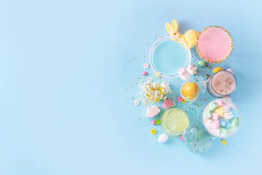 Colorful pastel colored kids Easter party mocktails, Creamy and iced non-alcohol drinks with cotton candy, marshmallow, sugar sprinkles and Easter eggs, on blue pink pastel background copy space