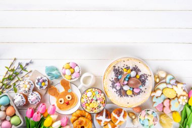 Easter brunch, breakfast food, Kids Easter party buffet. Various traditional Easter sweets, candy, pasties and baking - cross buns, cheesecake, chocolate eggs, pancakes, cupcakes, top view copy space