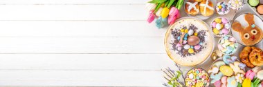 Easter brunch, breakfast food, Kids Easter party buffet. Various traditional Easter sweets, candy, pasties and baking - cross buns, cheesecake, chocolate eggs, pancakes, cupcakes, top view copy space