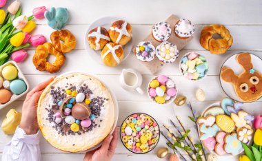 Easter brunch, breakfast food, Kids Easter party buffet. Various traditional Easter sweets, candy, pasties and baking - cross buns, cheesecake, chocolate eggs, pancakes, cupcakes, top view copy space