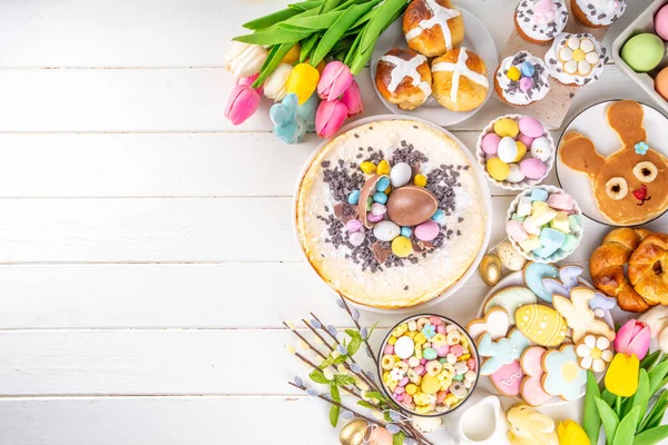 Easter brunch, breakfast food, Kids Easter party buffet. Various traditional Easter sweets, candy, pasties and baking - cross buns, cheesecake, chocolate eggs, pancakes, cupcakes, top view copy space