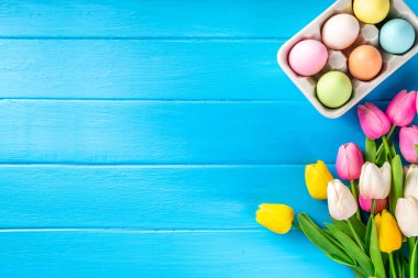 Simple minimal Easter greeting card background, colorful pastel Easter eggs with tulip flower bouquet, on light blue wooden plank background top view copy space