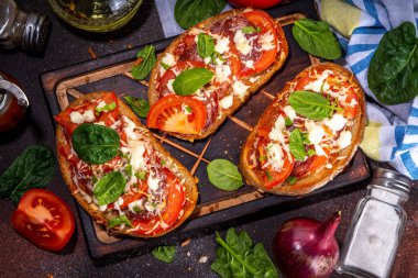 Hot loaded pizza sandwiches with tomatoes, mozzarella cheese and pepperoni, on dark background with herbs, olive oil and spices