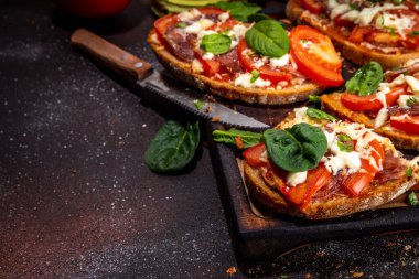 Hot loaded pizza sandwiches with tomatoes, mozzarella cheese and pepperoni, on dark background with herbs, olive oil and spices