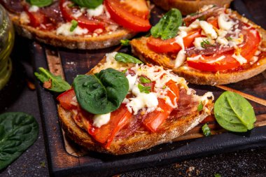 Hot loaded pizza sandwiches with tomatoes, mozzarella cheese and pepperoni, on dark background with herbs, olive oil and spices
