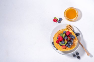 Healthy summer morning breakfast pancakes with fresh berry. Stack of traditional pancakes with blueberry, raspberries, honey. Healthy morning breakfast on white sunny background