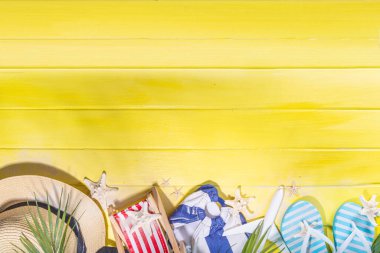 Bright sunny lighted summer vacation background, vacation and travel, beach accessories, swim suit, hat, flip flops, photo camera, sea star and shells on high-colored yellow wooden background top view