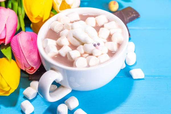 Funny Easter hot chocolate with Easter. Funny hot chocolate with easter symbols - rabbit feet, rabbit, flowers, marshmallow lamb. Cute cocoa recipe idea for Easter kids party