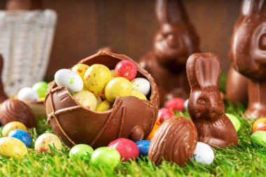 Easter egg hunting background. Various candy and chocolate Easter eggs, bunny and rabbits with basket for eggs on green grass park or garden background