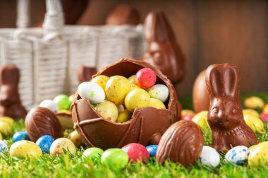 Easter egg hunting background. Various candy and chocolate Easter eggs, bunny and rabbits with basket for eggs on green grass park or garden background