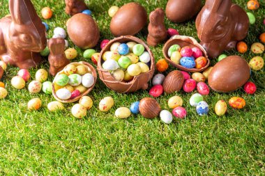 Paskalya yumurtası avcılığı geçmişi. Çeşitli şeker ve çikolatalı Paskalya yumurtası, tavşancık ve tavşanlar yeşil çimen parkında ya da bahçe arka planında yumurta sepeti