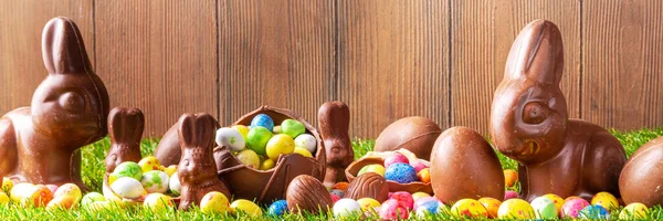 Easter egg hunting background. Various candy and chocolate Easter eggs, bunny and rabbits with basket for eggs on green grass park or garden background