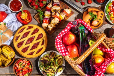 Çeşitli piknik barbekü yemekleri ve flatlay içiyorlar. Yaz bbq piknik yemekleri, ızgara etler, kebaplar, sebzeler, meyve salatası, geleneksel piknik pastası, sandviçler, üst görünüm fotokopi alanı.