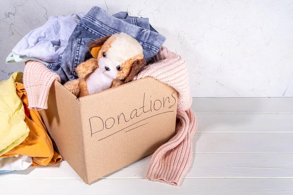 Giysileri, oyuncakları ve yiyeceği beyaz masa arkasında olan bağış kutusu. Oyuncak, kadın ve çocuk kıyafetleri ve yiyeceklerle dolu bir karton bağış kutusu. Sosyal hizmet, gönüllülük, yardım konsepti kopyalama alanı