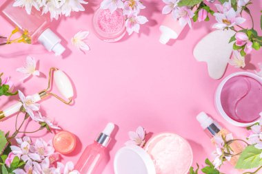 Spring skin care cosmetics flat lay.  Beauty facial care cosmetics: serum, cream, mask on pink sunny background with spring blossom flowers, top view copy space