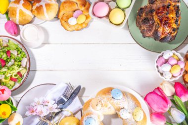 Festivalde Paskalya yemeği veya brunch masası sunuldu, Paskalya yumurtası, lale çiçeği buketi, geleneksel Paskalya yemekleri - pasta, çapraz çörekler, çelenk ekmeği, jöleli jambon ve bahar salatası, beyaz masa arkaplanı